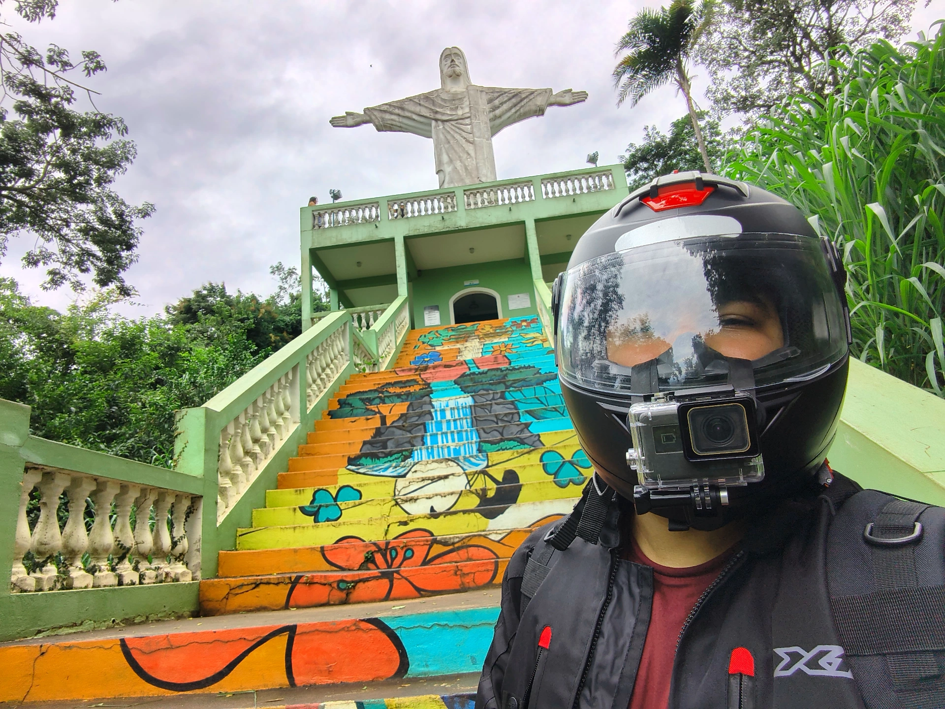 Selfie de capacete com GoPro em frente ao Cristo de São Pedro, com a escadaria colorida grafitada ao fundo