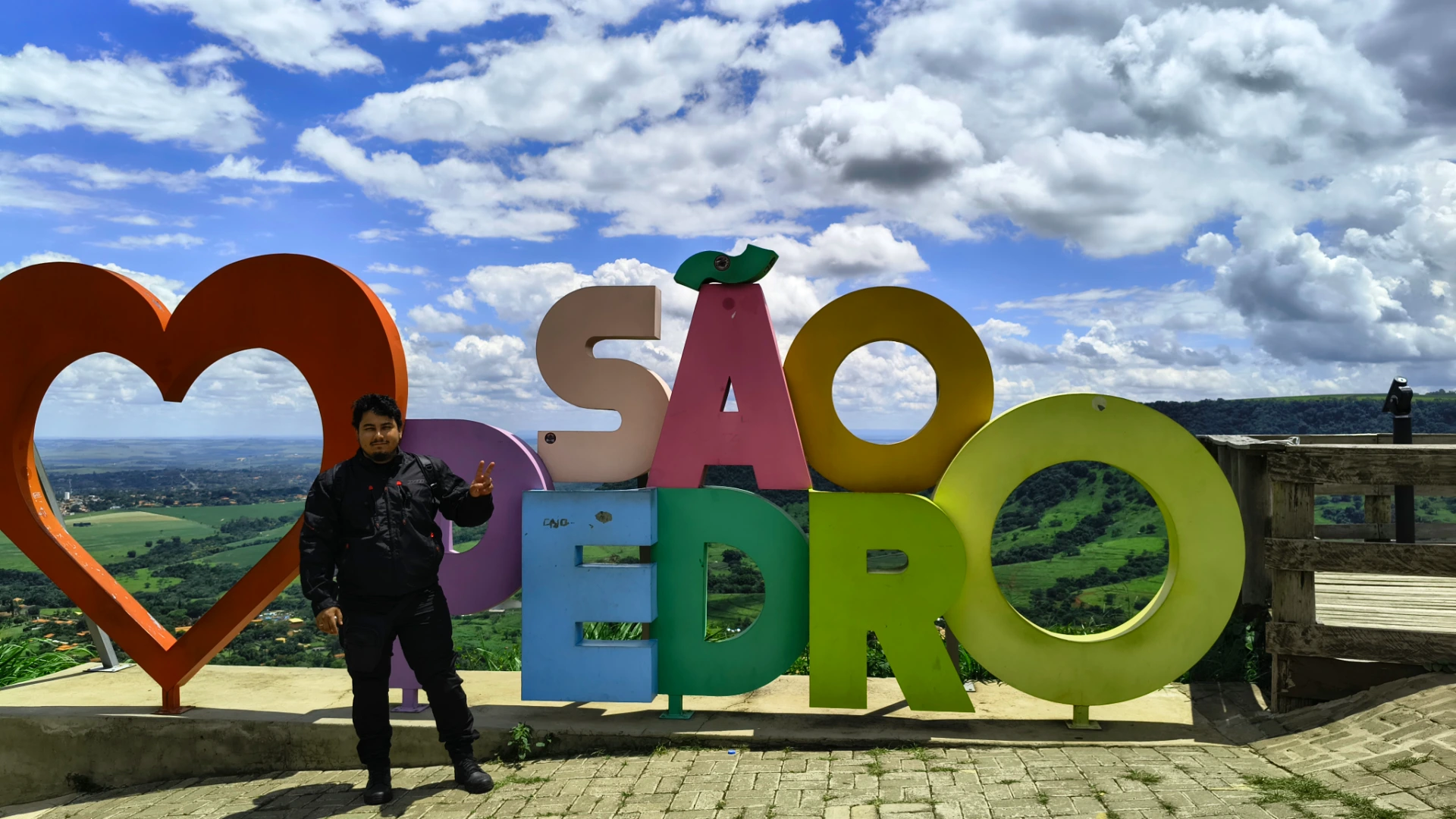 Motociclista de jaqueta preta ao lado do letreiro Eu amo São Pedro no mirante da Serra de São Pedro