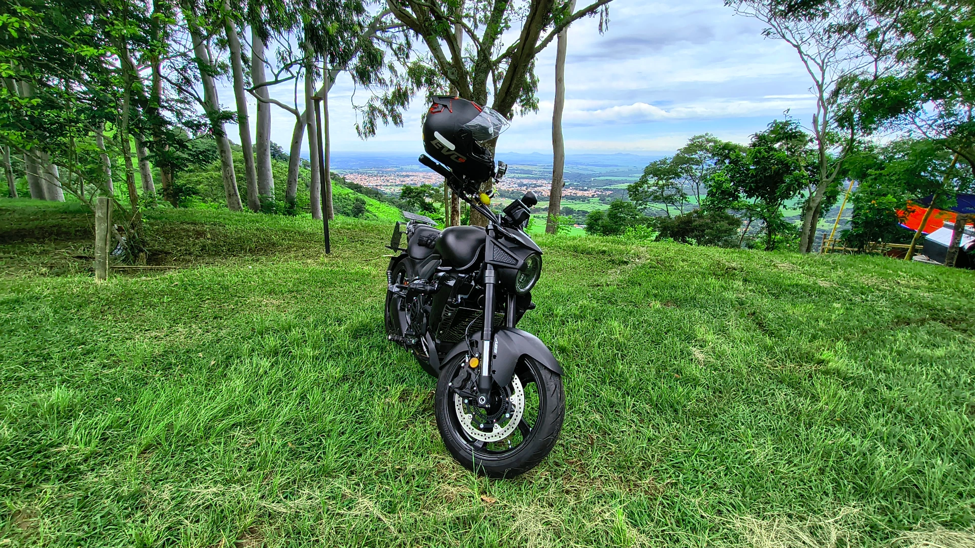 Moto estacionada no gramado da Serra de São Pedro, com capacete apoiado no guidão e vista da cidade ao fundo